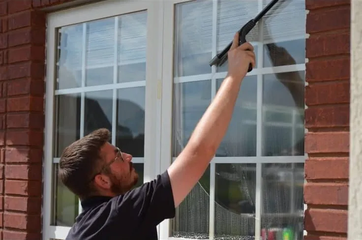 HoneyBee technician squeegeeing a window streak-free on a brick home