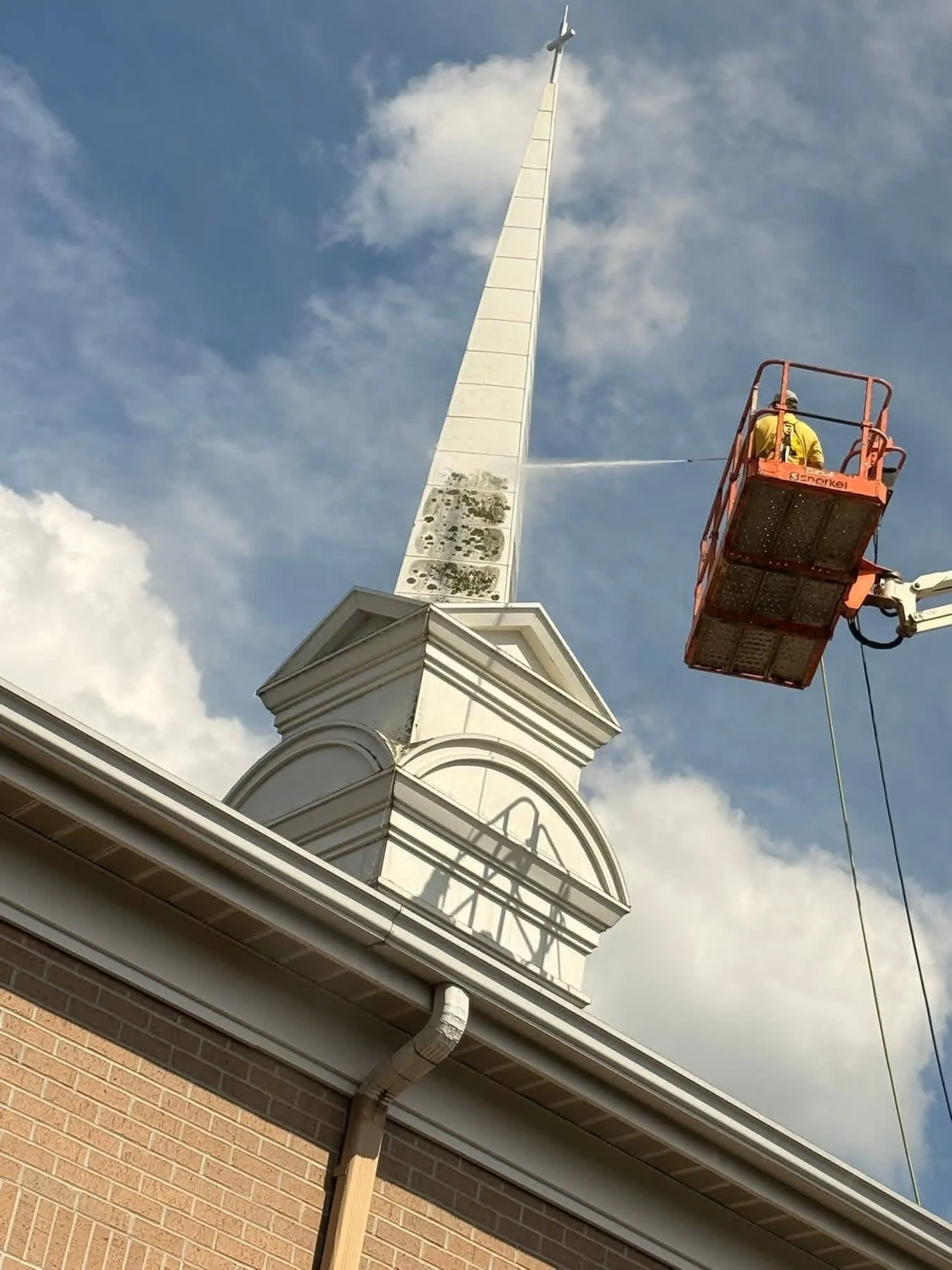 HoneyBee technician in a boom lift soft-washing algae from a church steeple